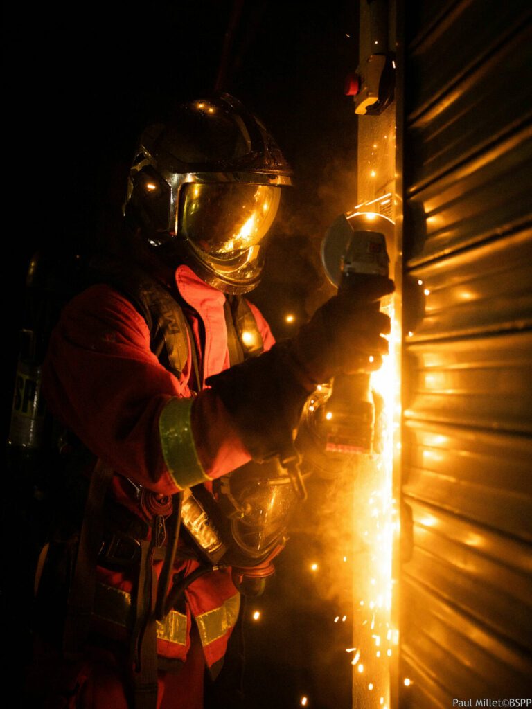 Les sapeurs-pompiers de Paris découpent à la disqueuse un rideau de fer pour trouver le foyer de l'incendie